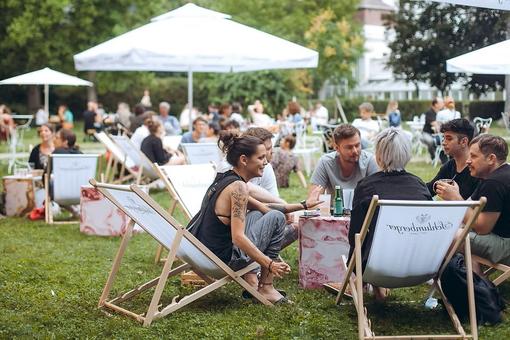 The photo shows a scene in a park: people sitting in deckchairs, under parasols and enjoying drinks