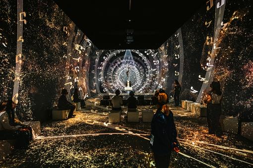 Ausstellungsraum im Johann Strauss Museum - New Dimensions mit Strauss-Statue und abstrakten Musik-Visuals, darunter auch Notenzeilen sowie Besucher:innen.